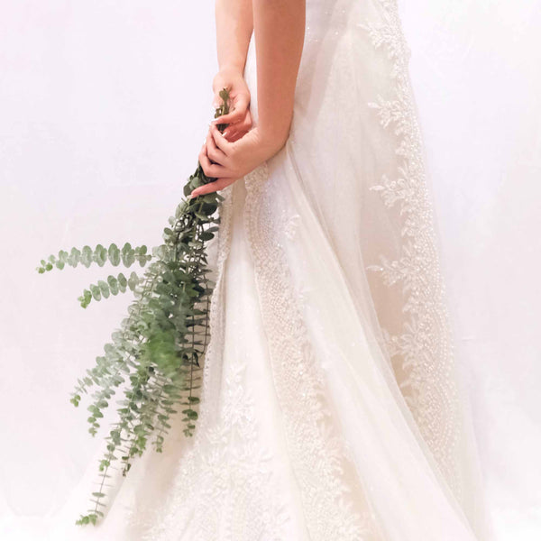 bride holding eucalyptus behind back in white dress